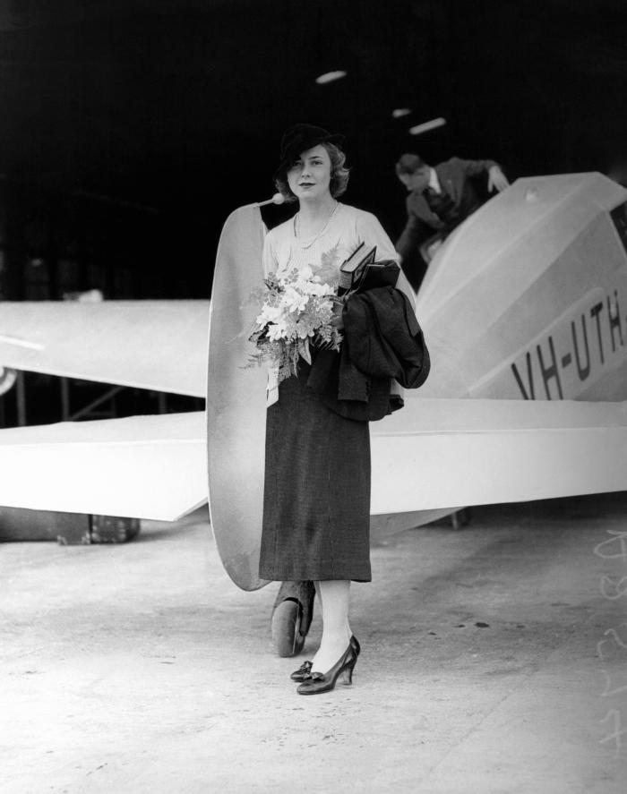 The Monospar provides the backdrop to Helen Hughes, daughter of the Rt Hon W. M. Hughes and Dame Mary Hughes, as she arrives in Brisbane during March 1936 for a series of fur fashion parades sponsored by the Lambs department store.